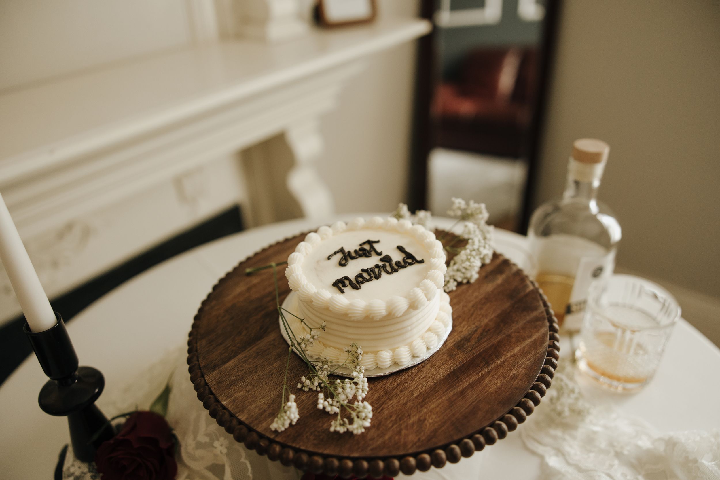 Small white wedding cake on wooden stand with simple decorative elements.