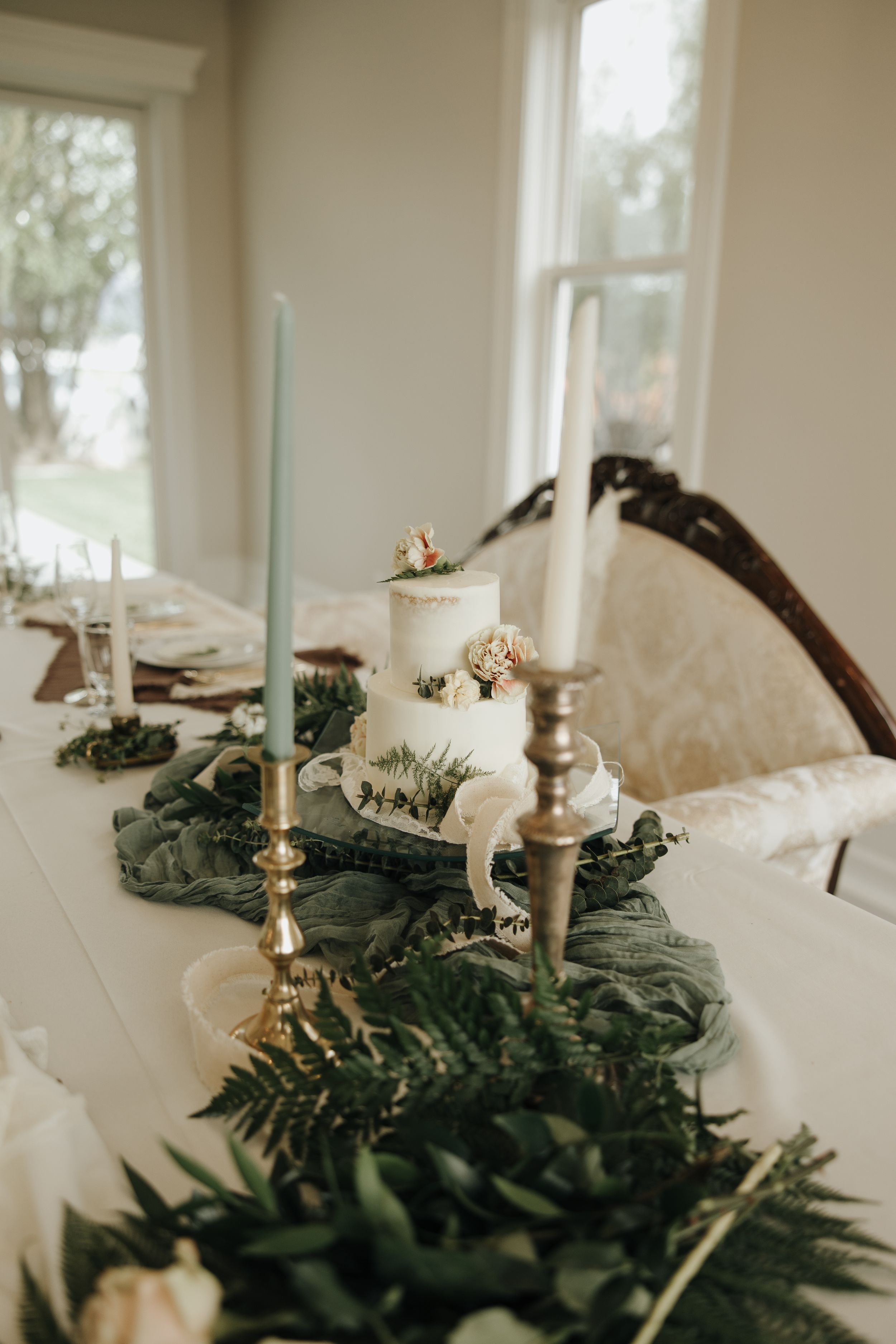 Elegant table setting with white candles, greenery runner and silver candlesticks.