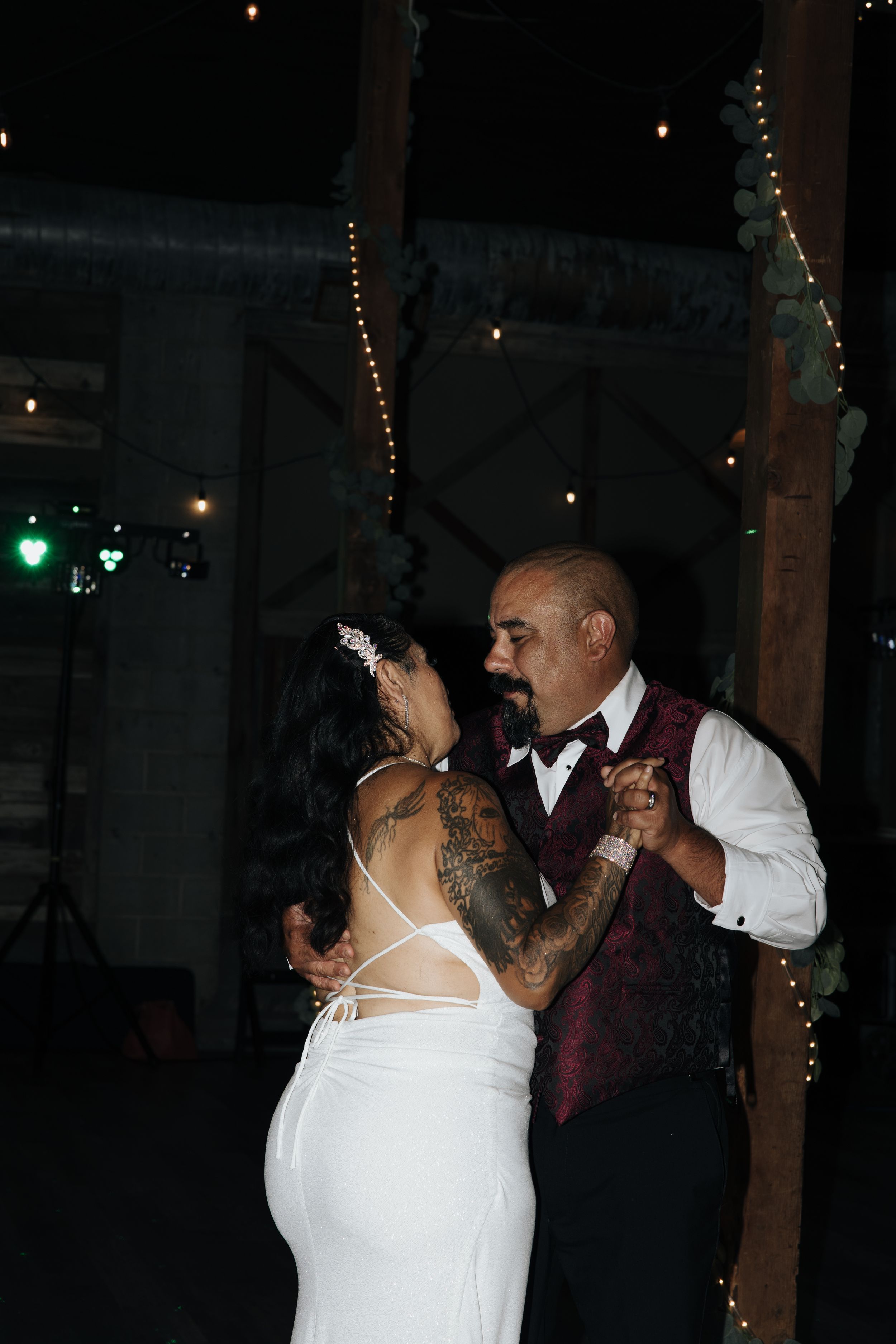 Couple dancing intimately at evening reception with string lights.
