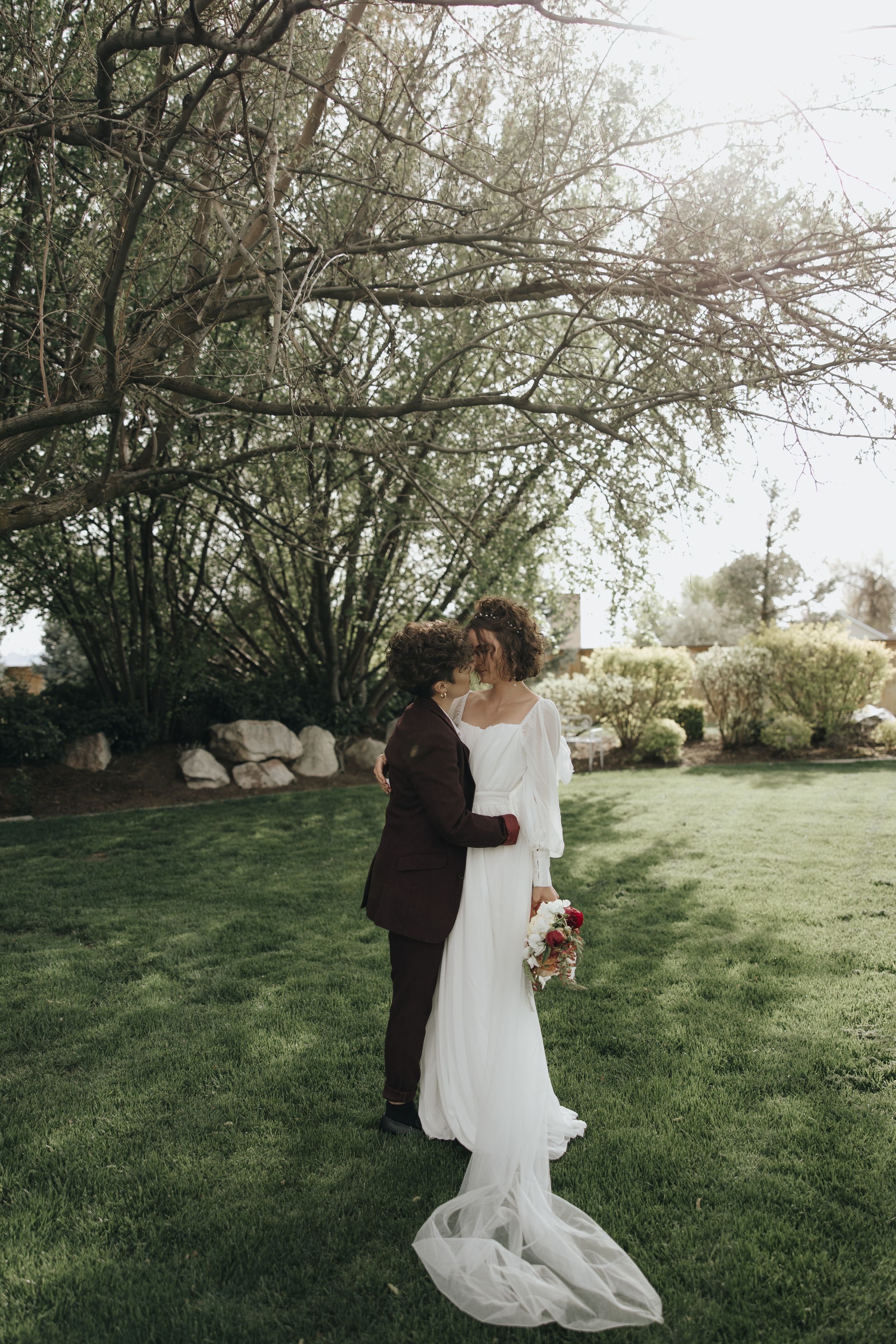 Wedding couple embraces in garden setting with flowing white dress and formal attire.