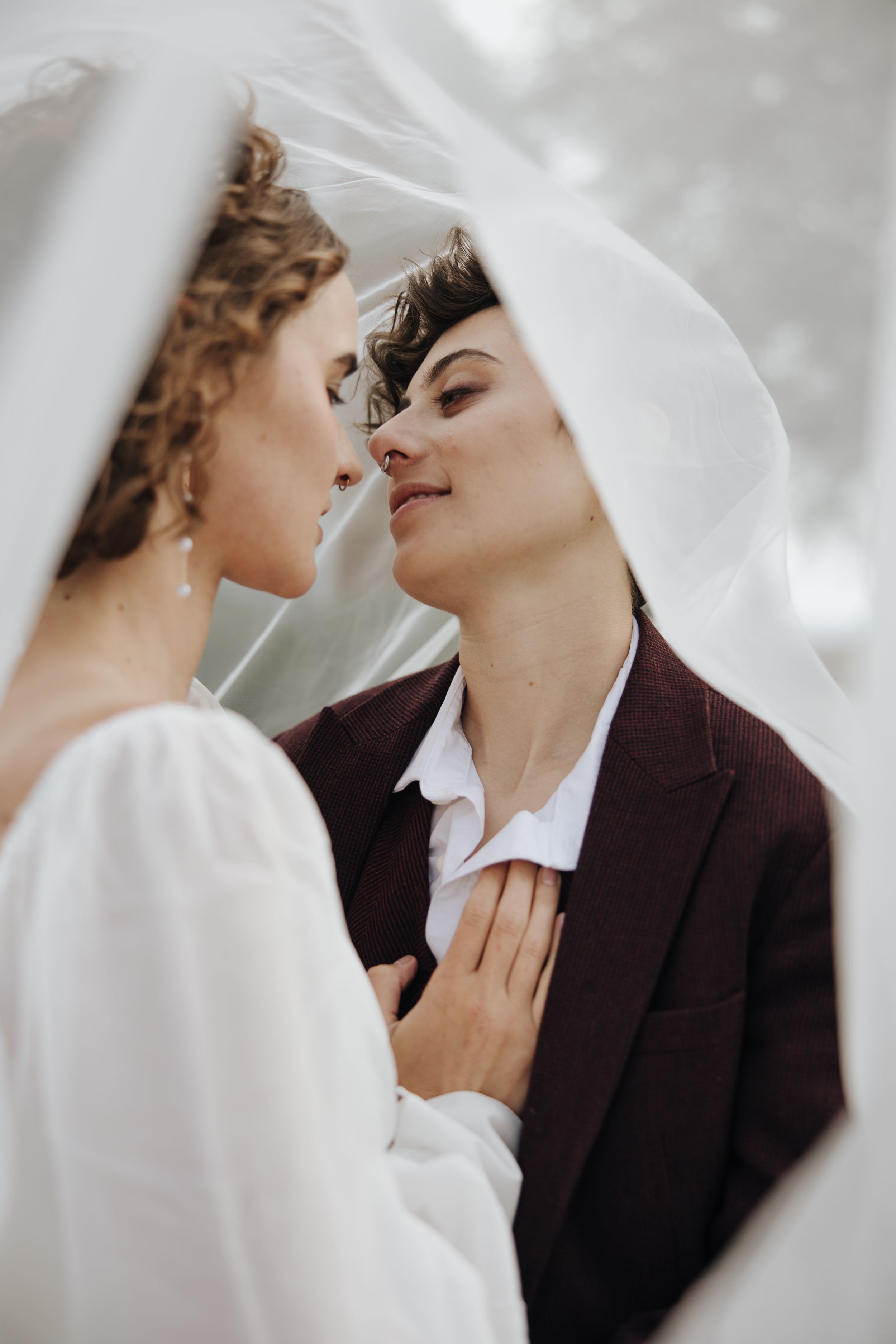 A romantic moment under a delicate white veil with a person in a burgundy suit and white shirt.