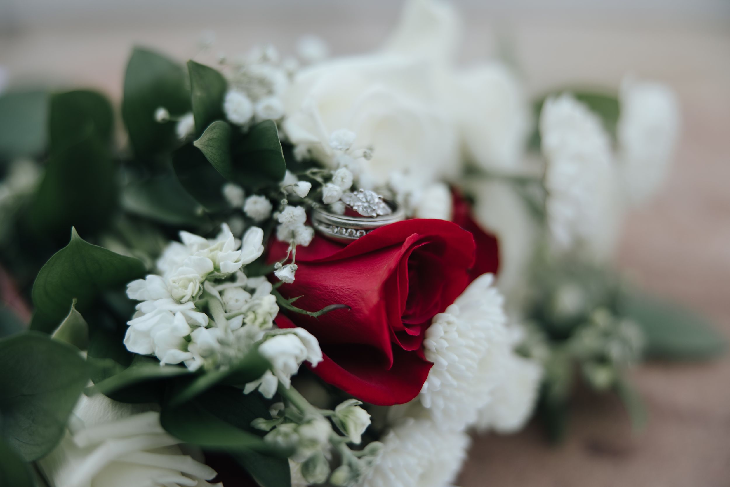 Close-up of wedding bouquet featuring red rose with white flowers and green foliage.