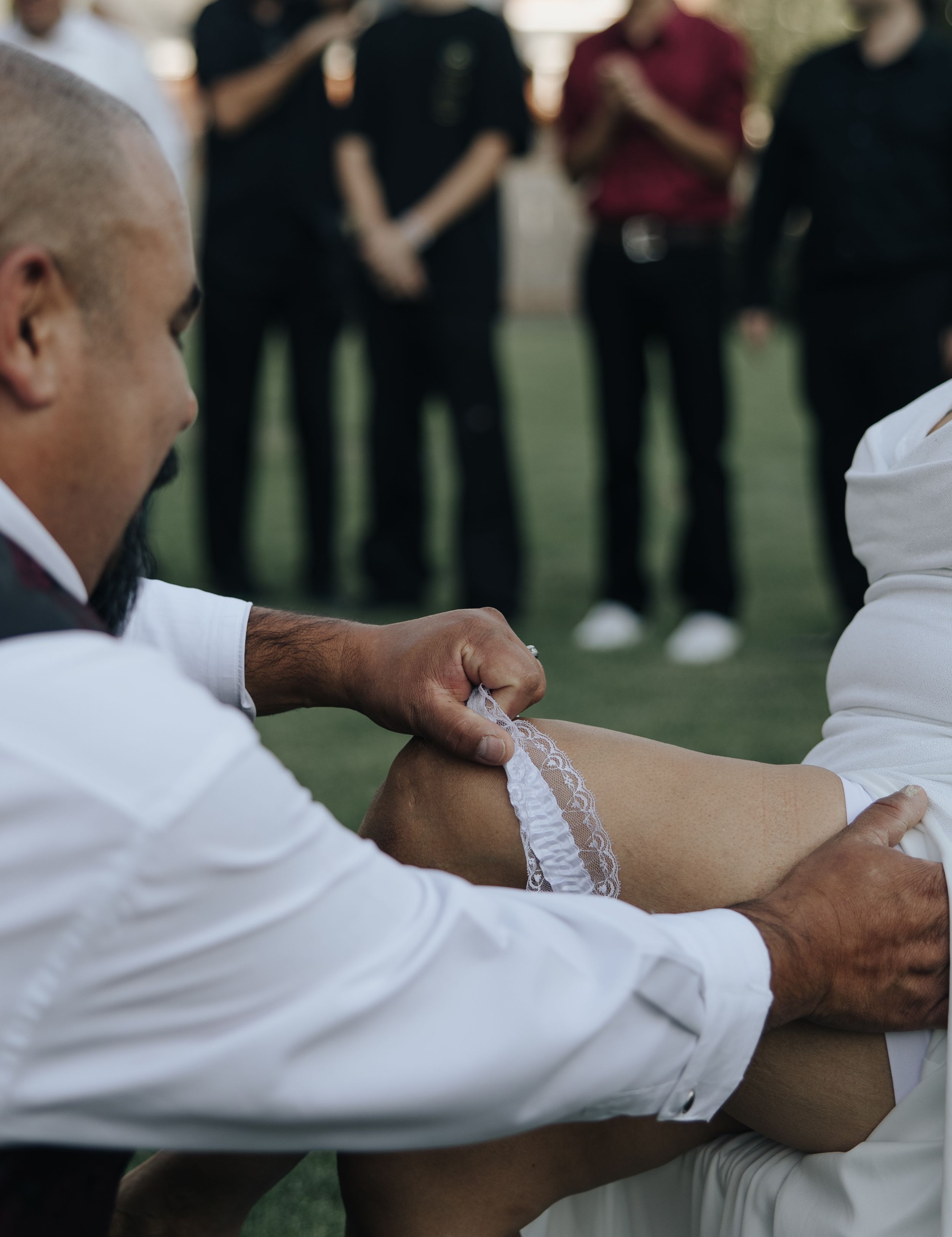 Close up of garter removal tradition during outdoor wedding reception.