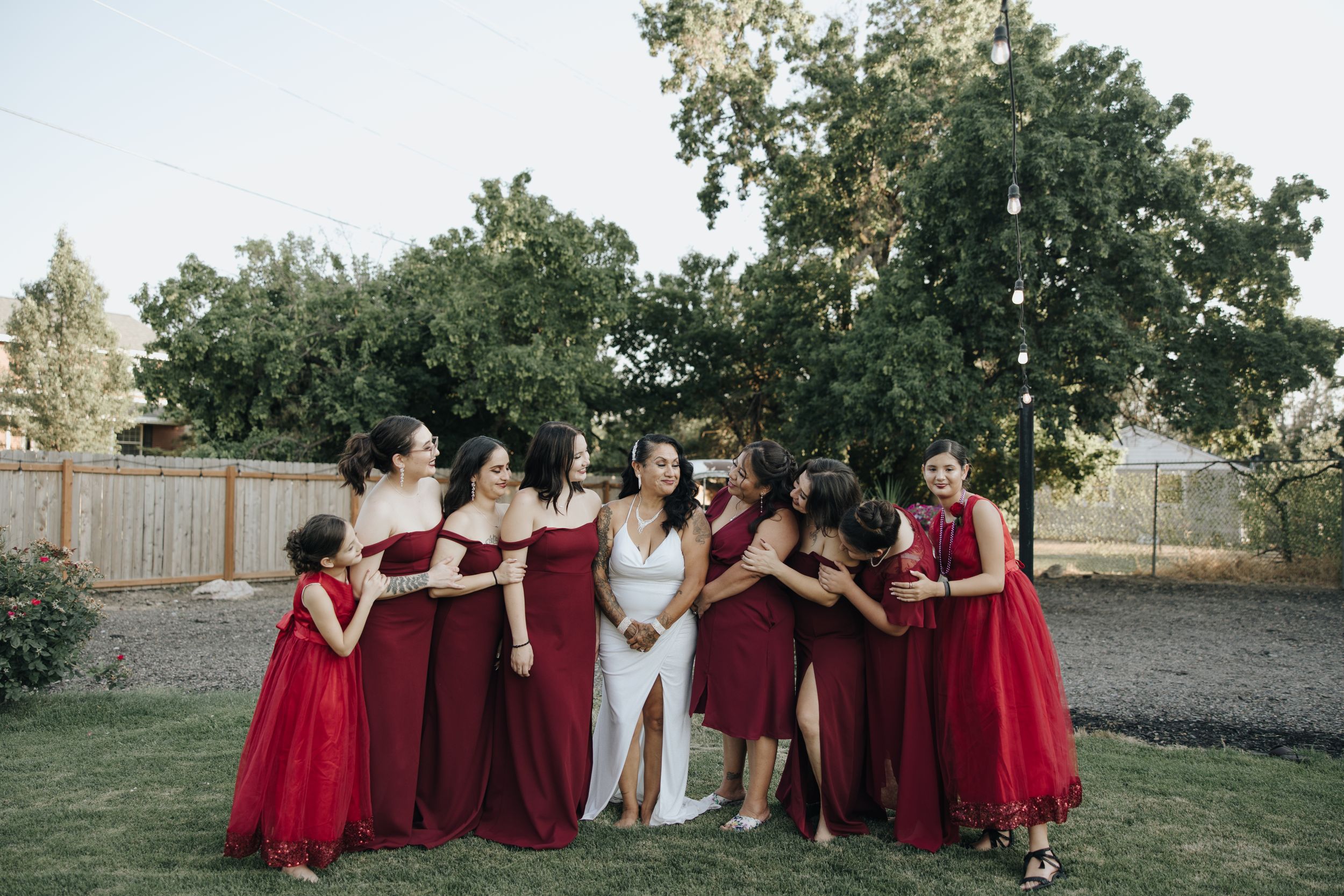 Wedding party in burgundy bridesmaid dresses poses together outdoors.