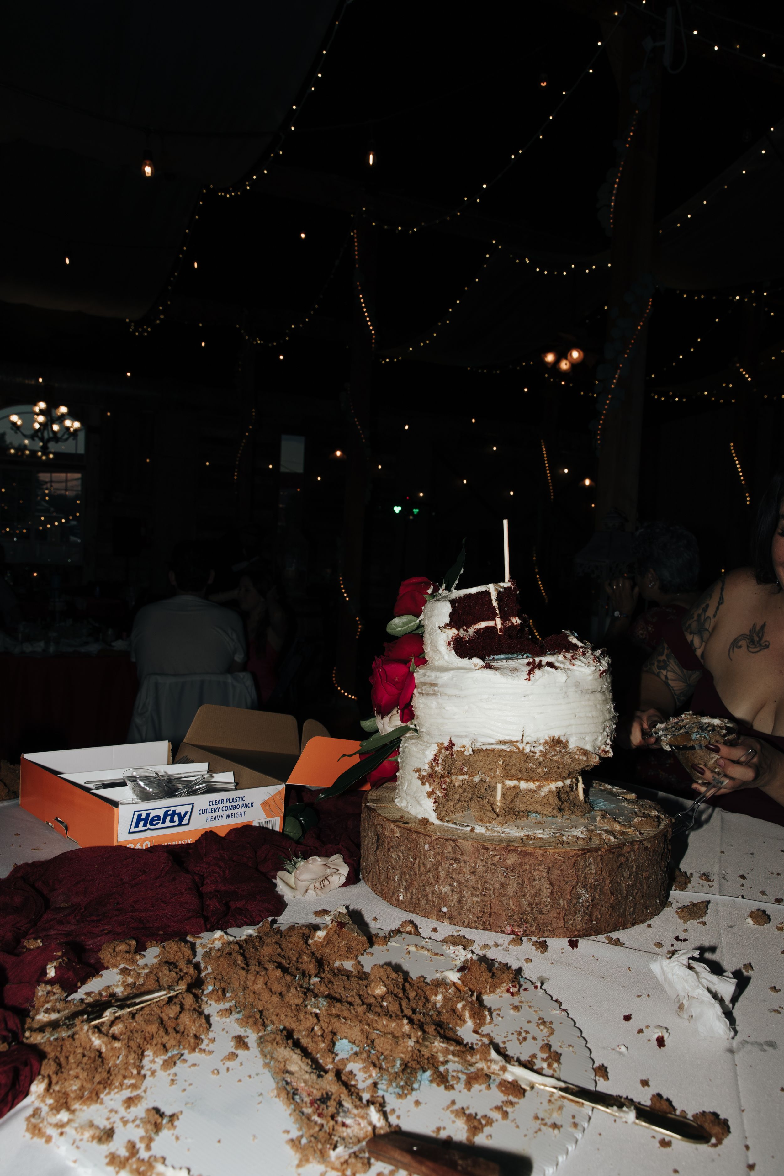 Messy wedding cake and dessert table at nighttime reception with string lights.