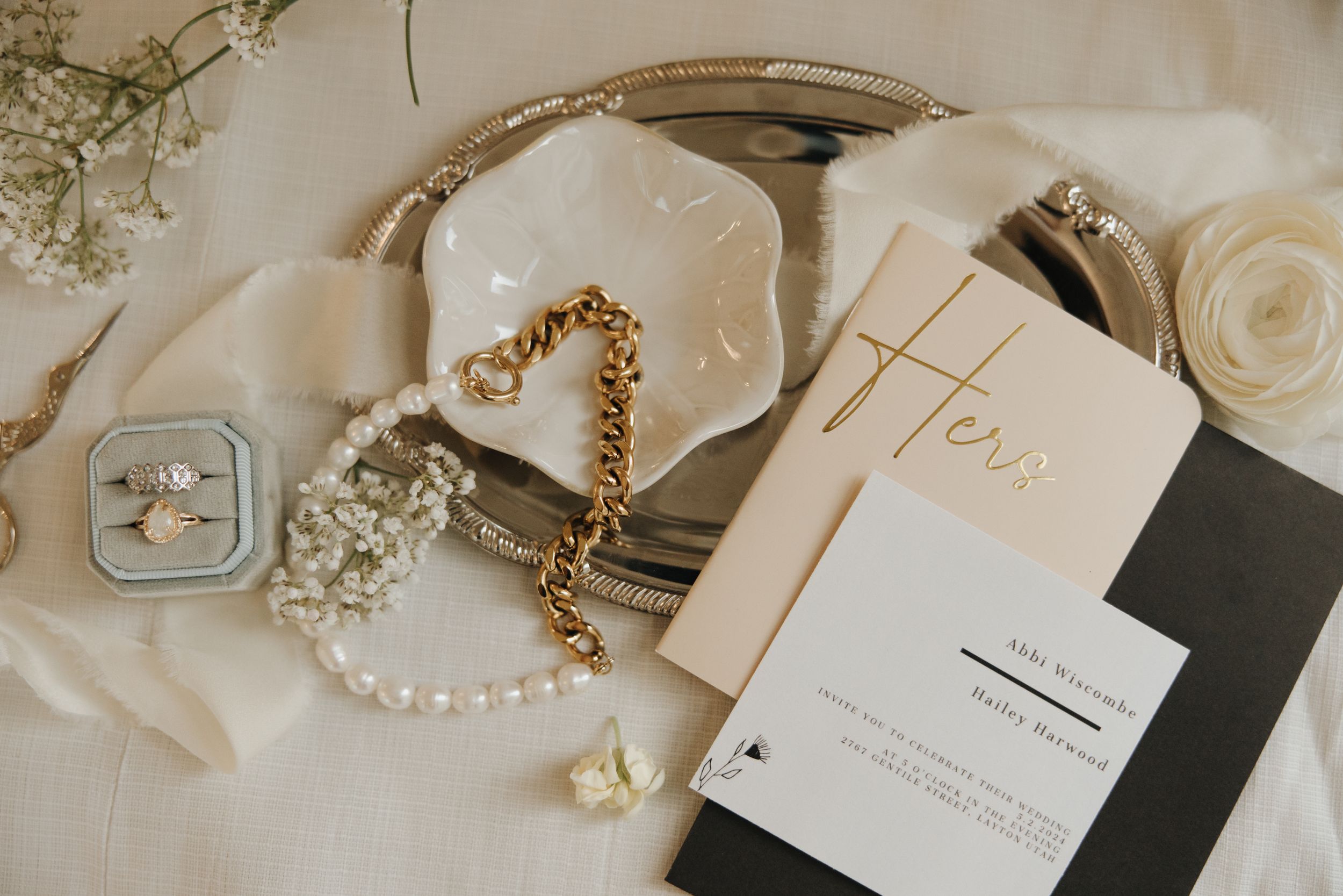 Wedding details flatlay with invitation, jewelry and ring box on white fabric.