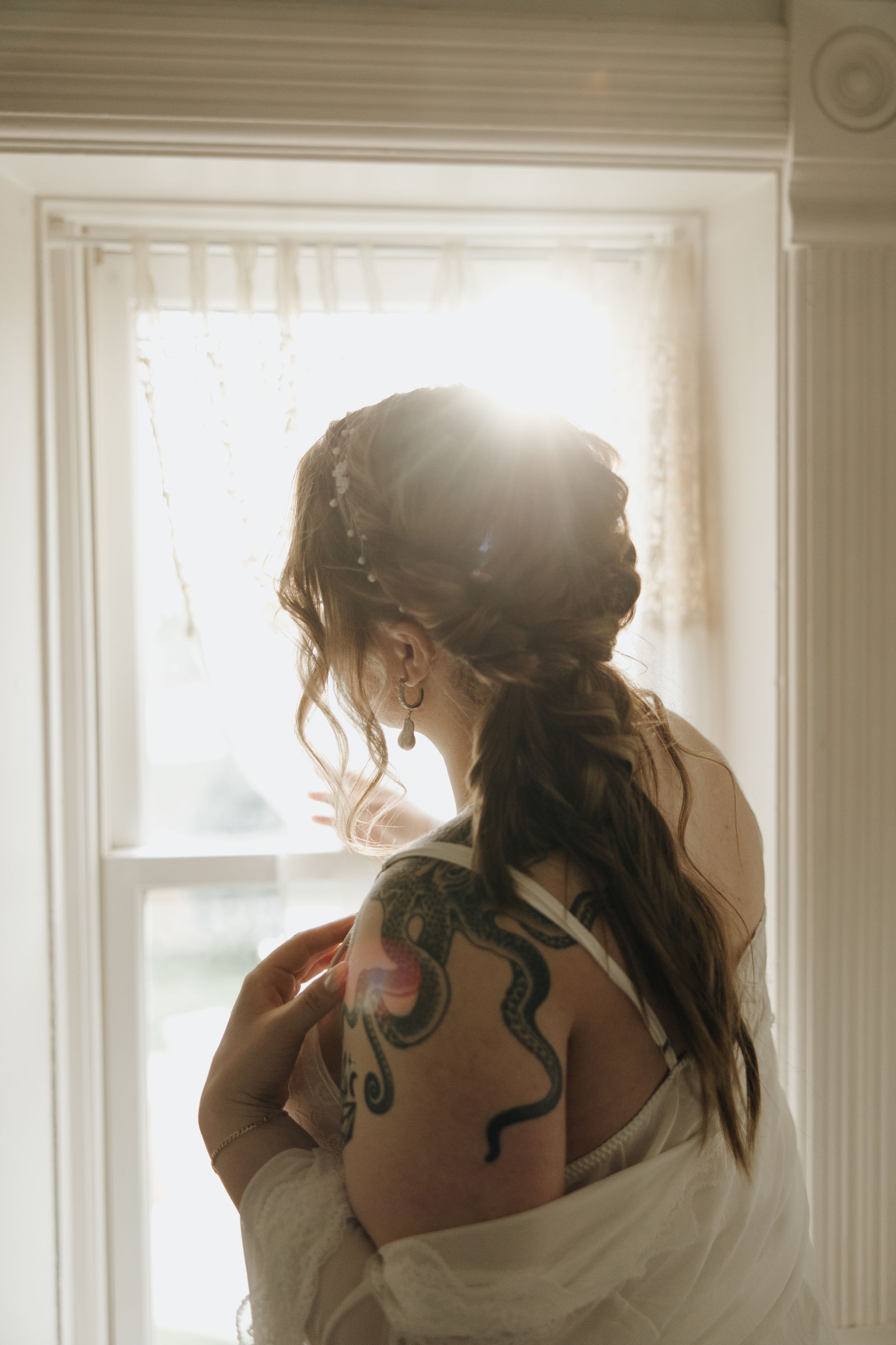 Silhouetted figure in front of window displays intricate snake tattoo on bare shoulder in soft light.