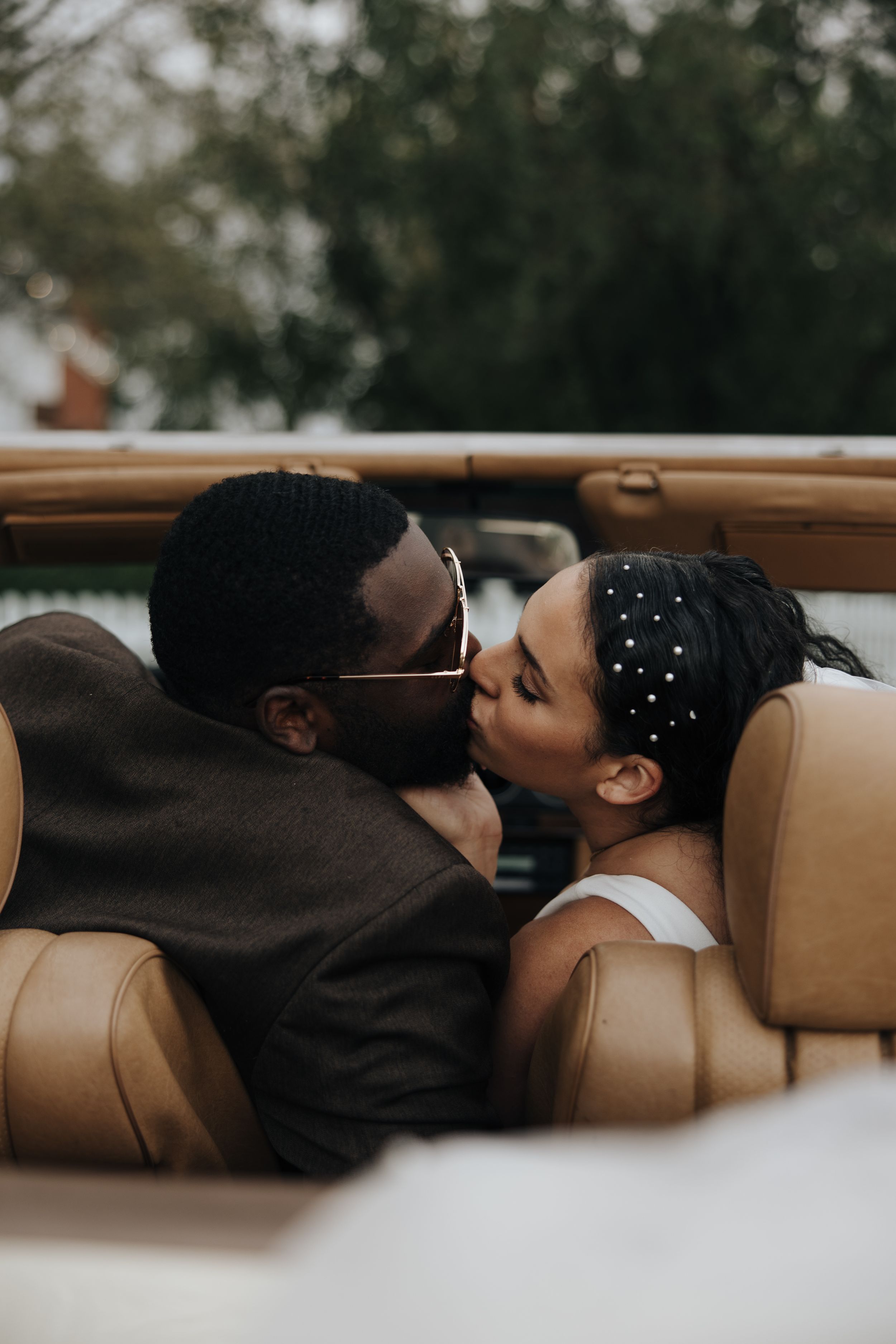 Romantic couple sharing intimate moment in luxury convertible car with tan leather seats.