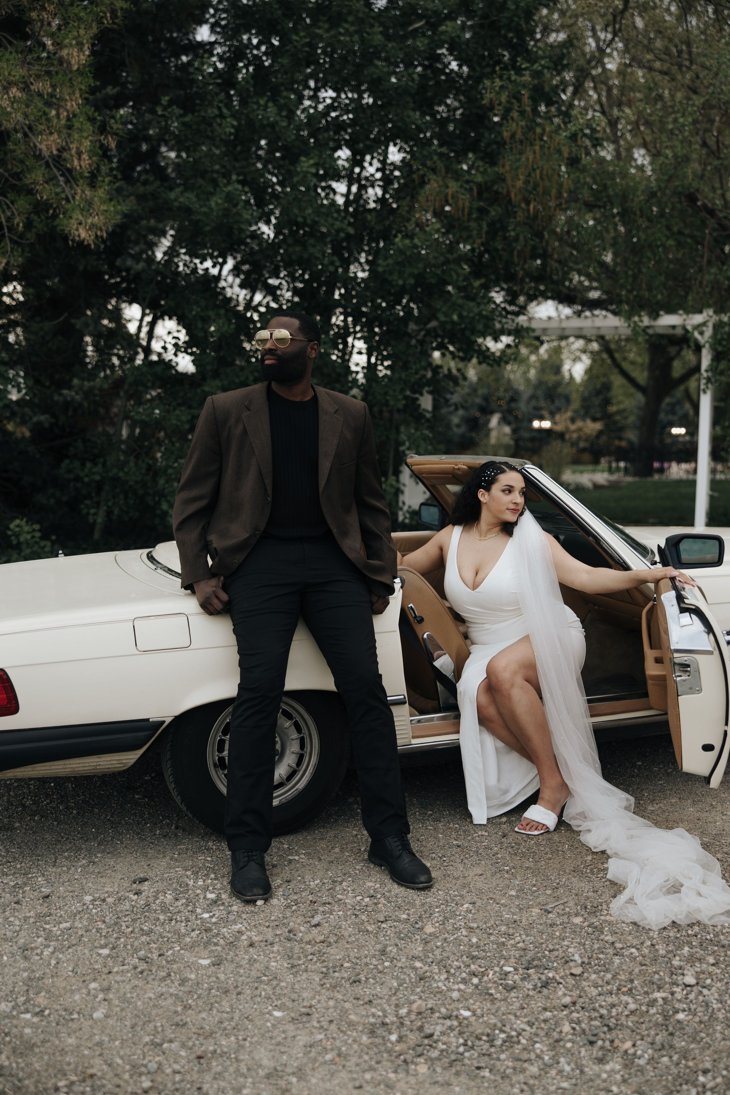 Couple poses elegantly by vintage white car, contrasting formal wear and casual poses.