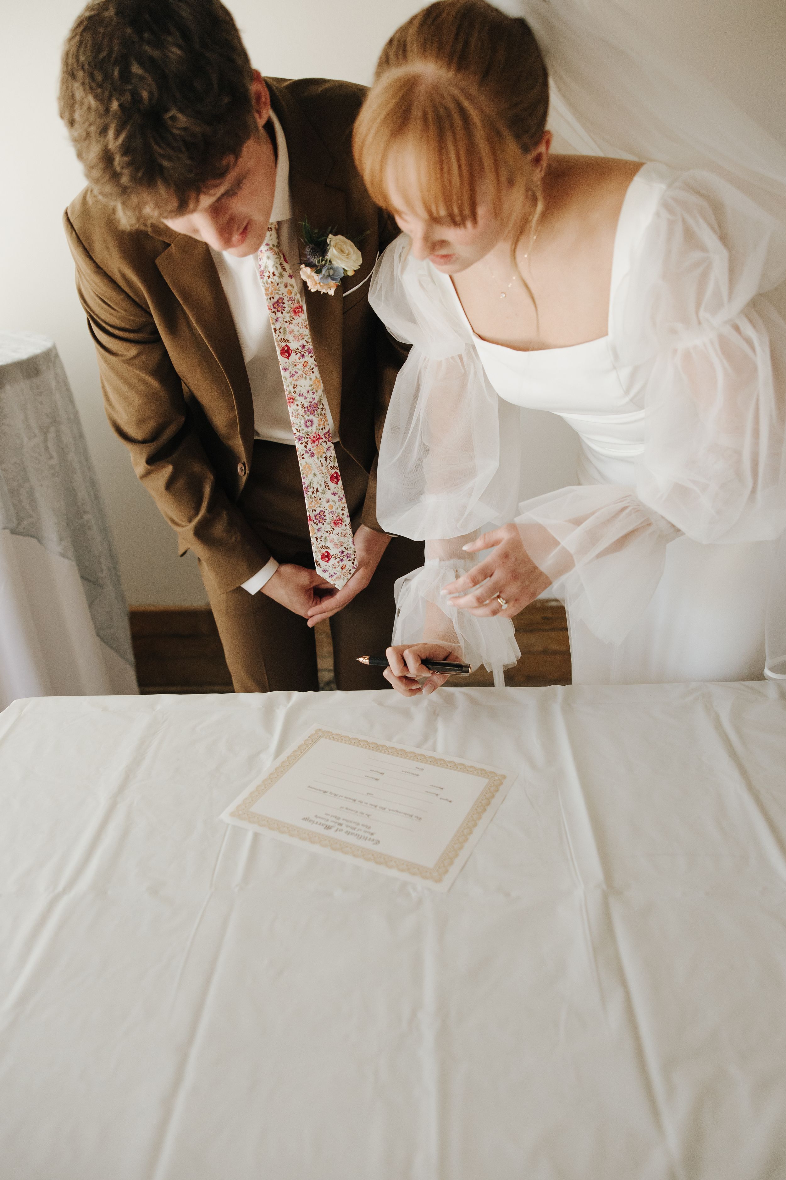 Couple signs marriage certificate together in formal attire.