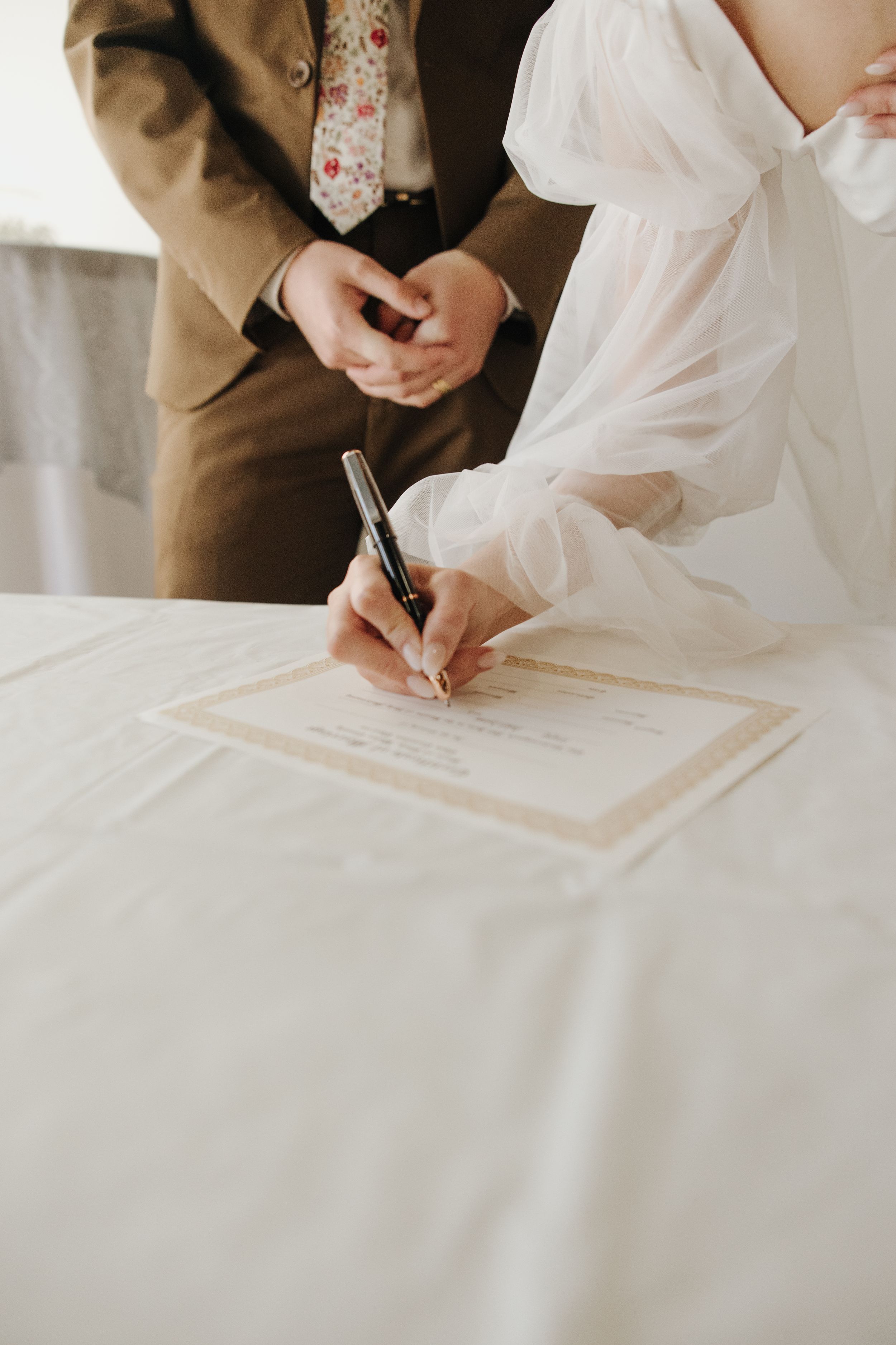 Bride signing marriage documents with fountain pen during wedding ceremony.