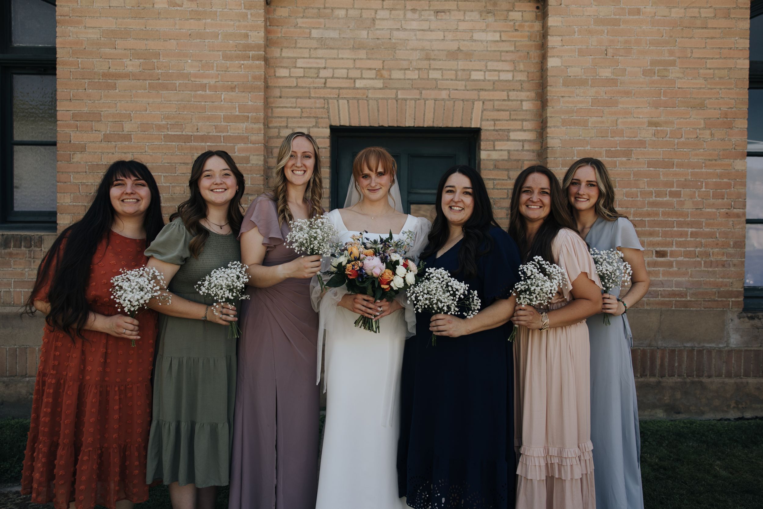 Wedding party posing against brick wall in coordinated dusty tones.