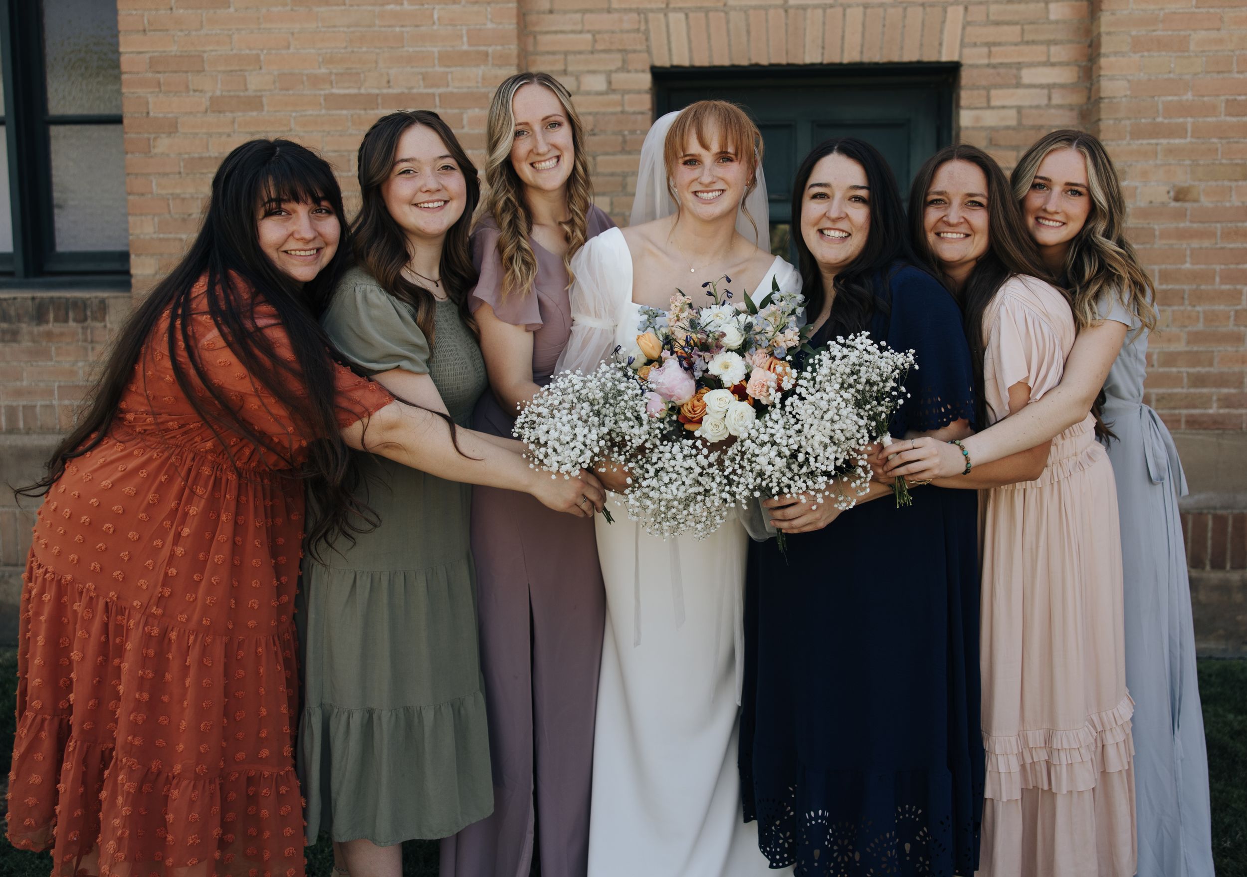 Bridal party in mix-and-match dresses holding bouquets together.