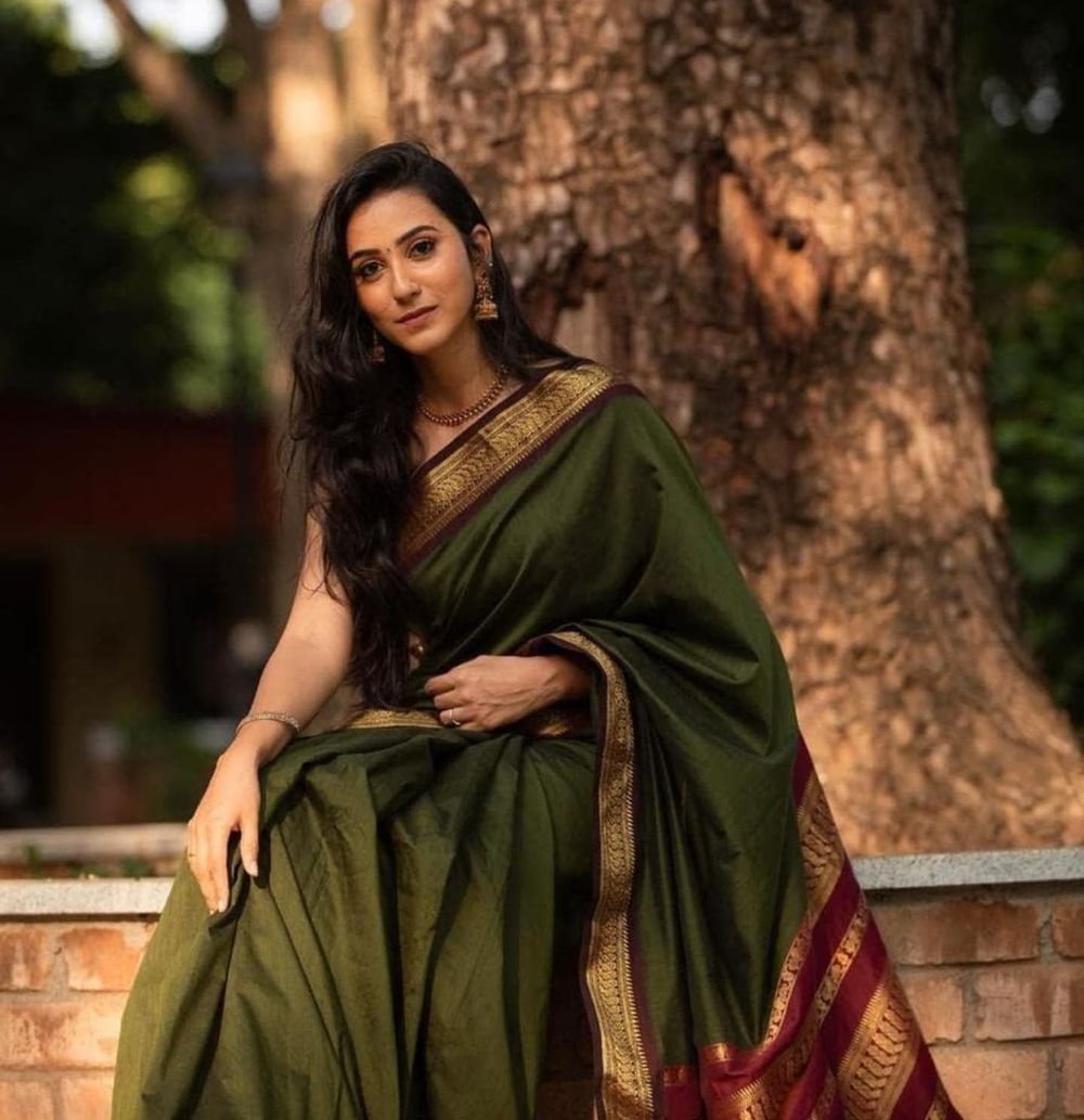 A forest green silk saree with traditional border design photographed outdoors by a tree.