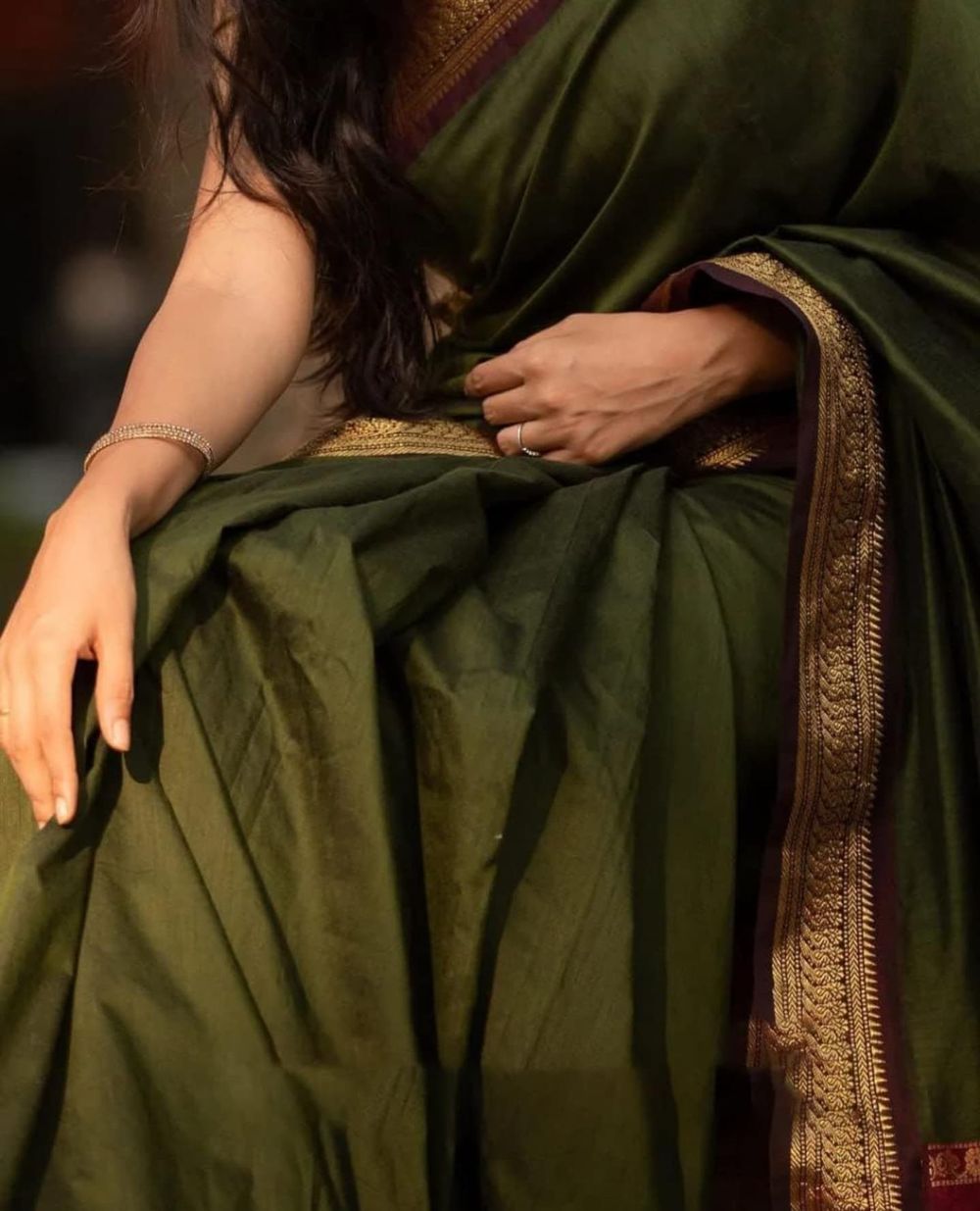 Close-up detail of a dark green saree with intricate gold border design.