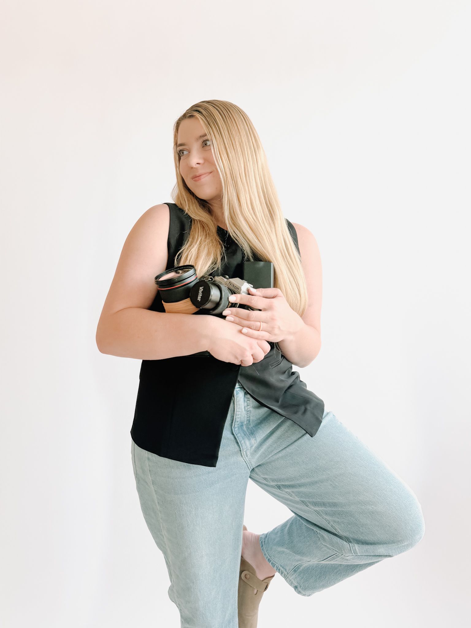 A photographer in a cream sweater holds a camera while sitting against a white background.