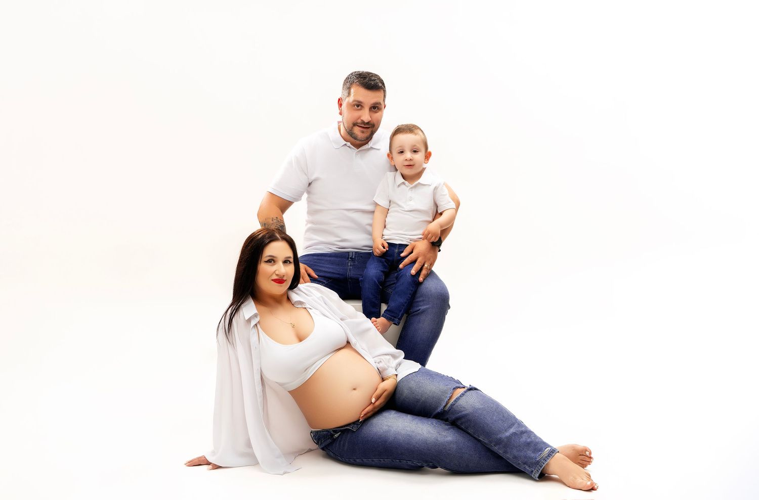 A maternity photo featuring an expectant mother in white resting on the floor with loved ones beside her.