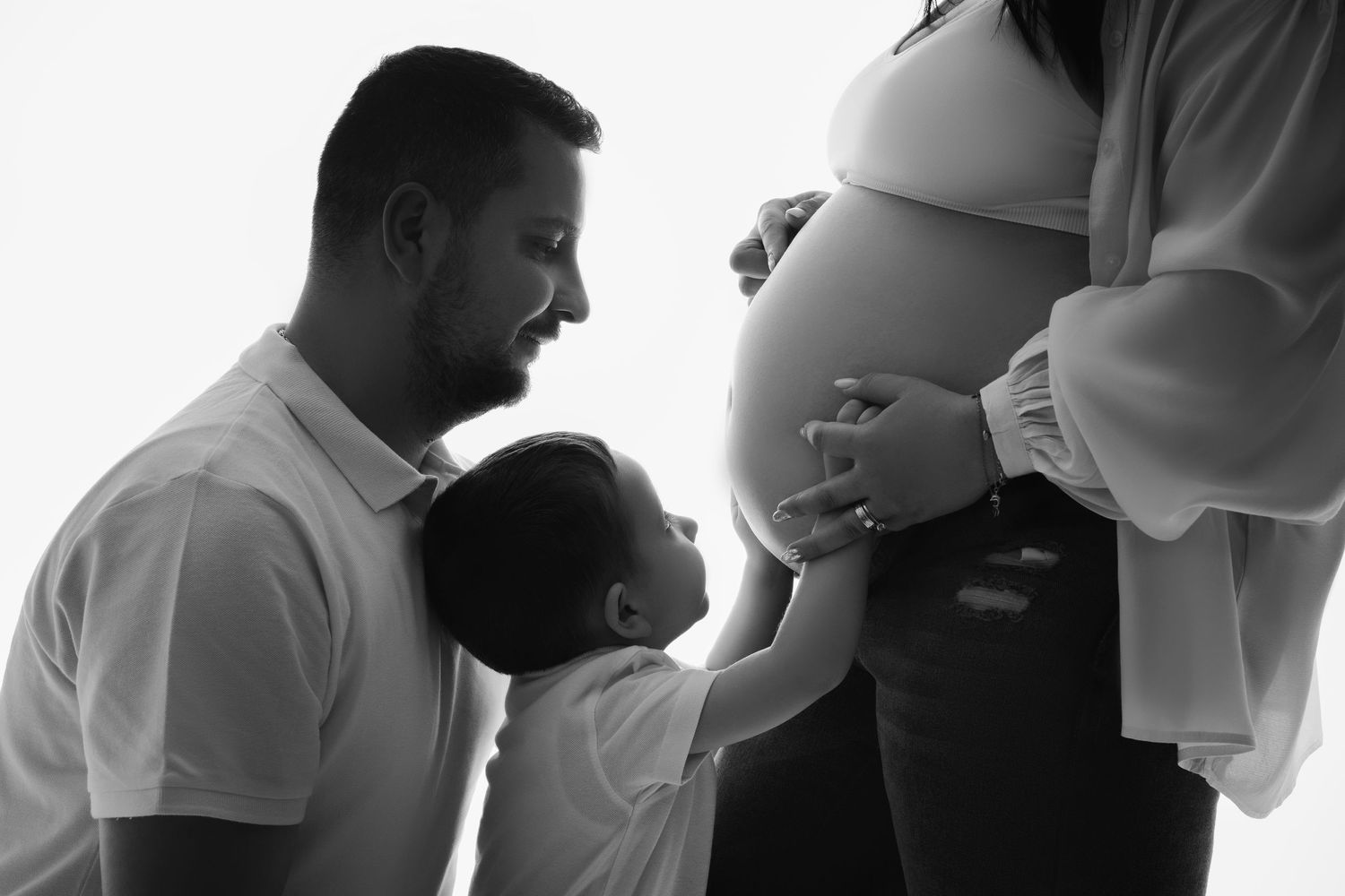 Black and white photo showing tender family moment with pregnant belly and touching hands together.