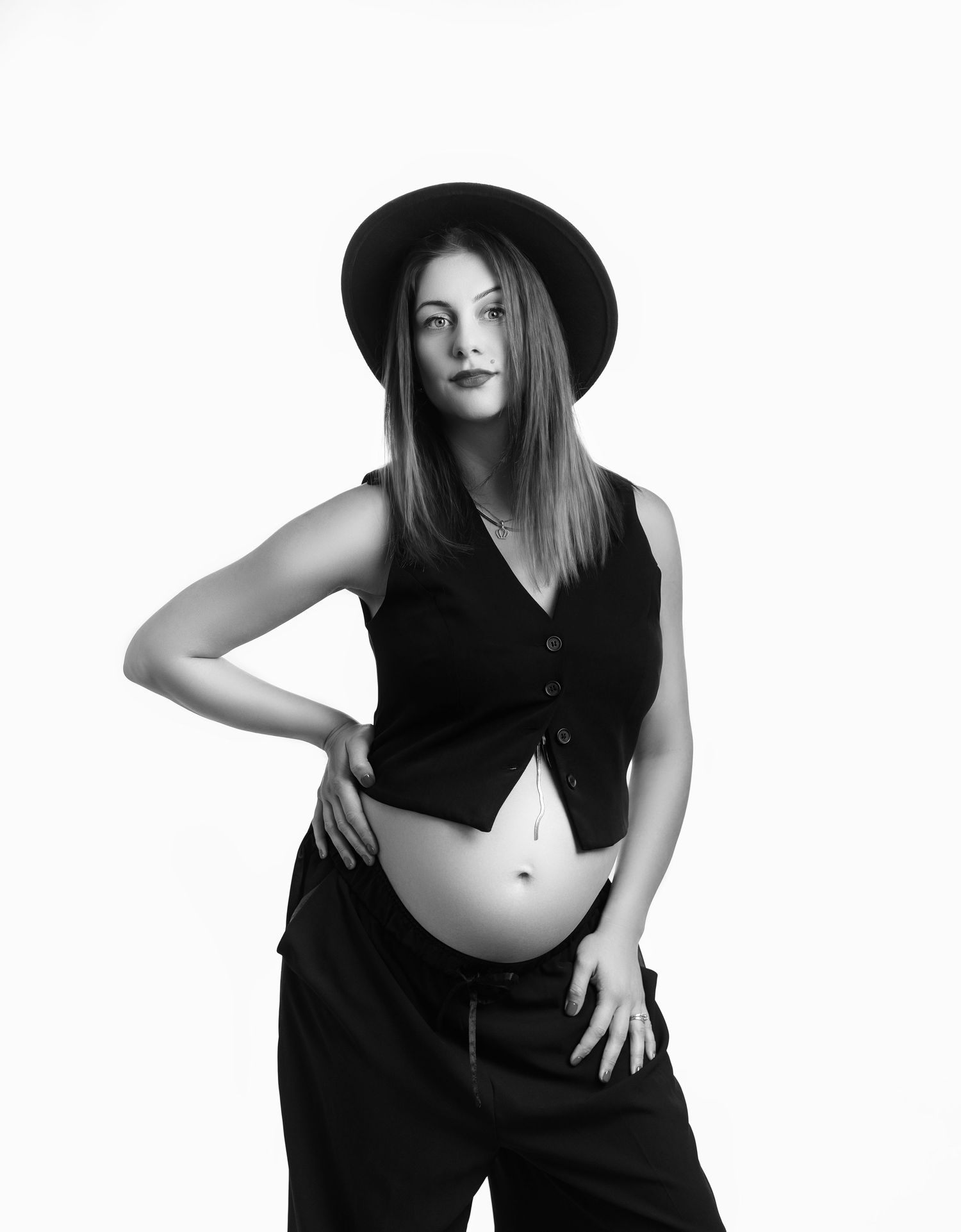 Black and white studio portrait showing a model in a cropped vest and wide-leg pants striking a confident pose.