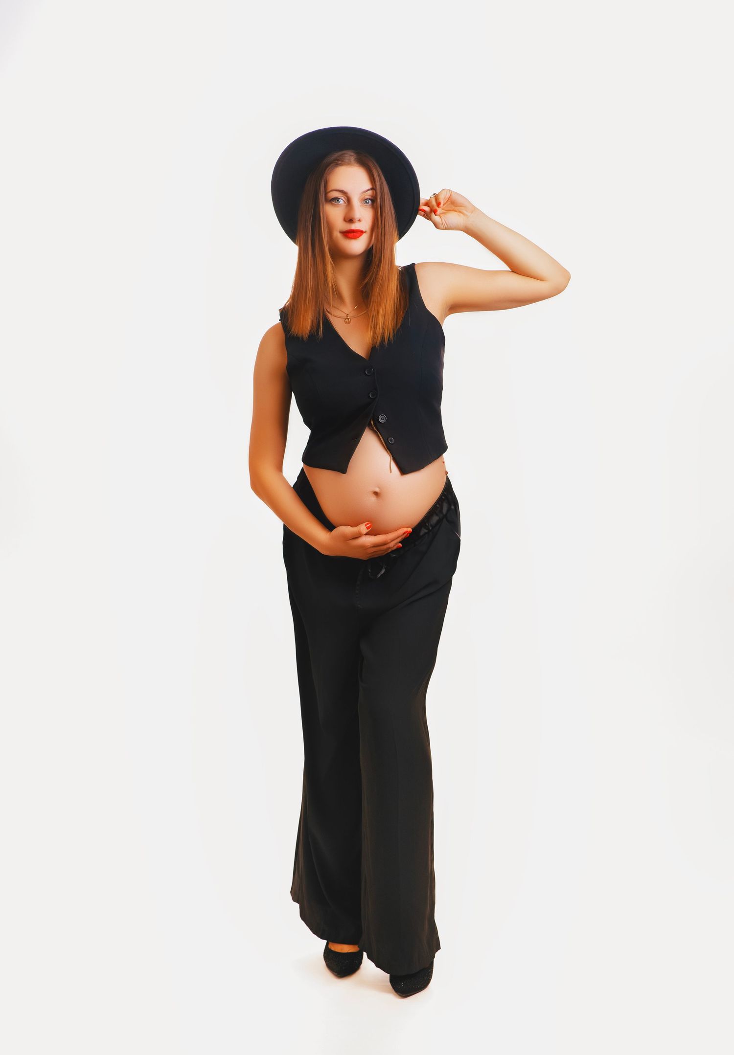 A person in all black attire featuring a wide-brimmed hat, cropped top and flared pants poses against a white background.