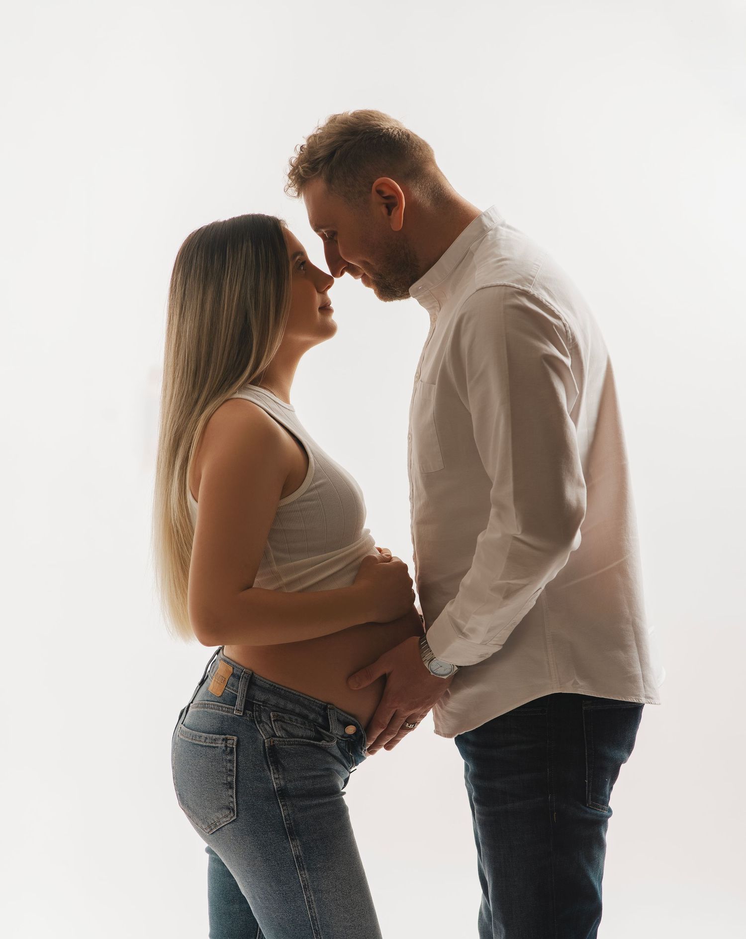 A romantic maternity photograph showing an intimate moment between a couple illuminated by soft backlighting.