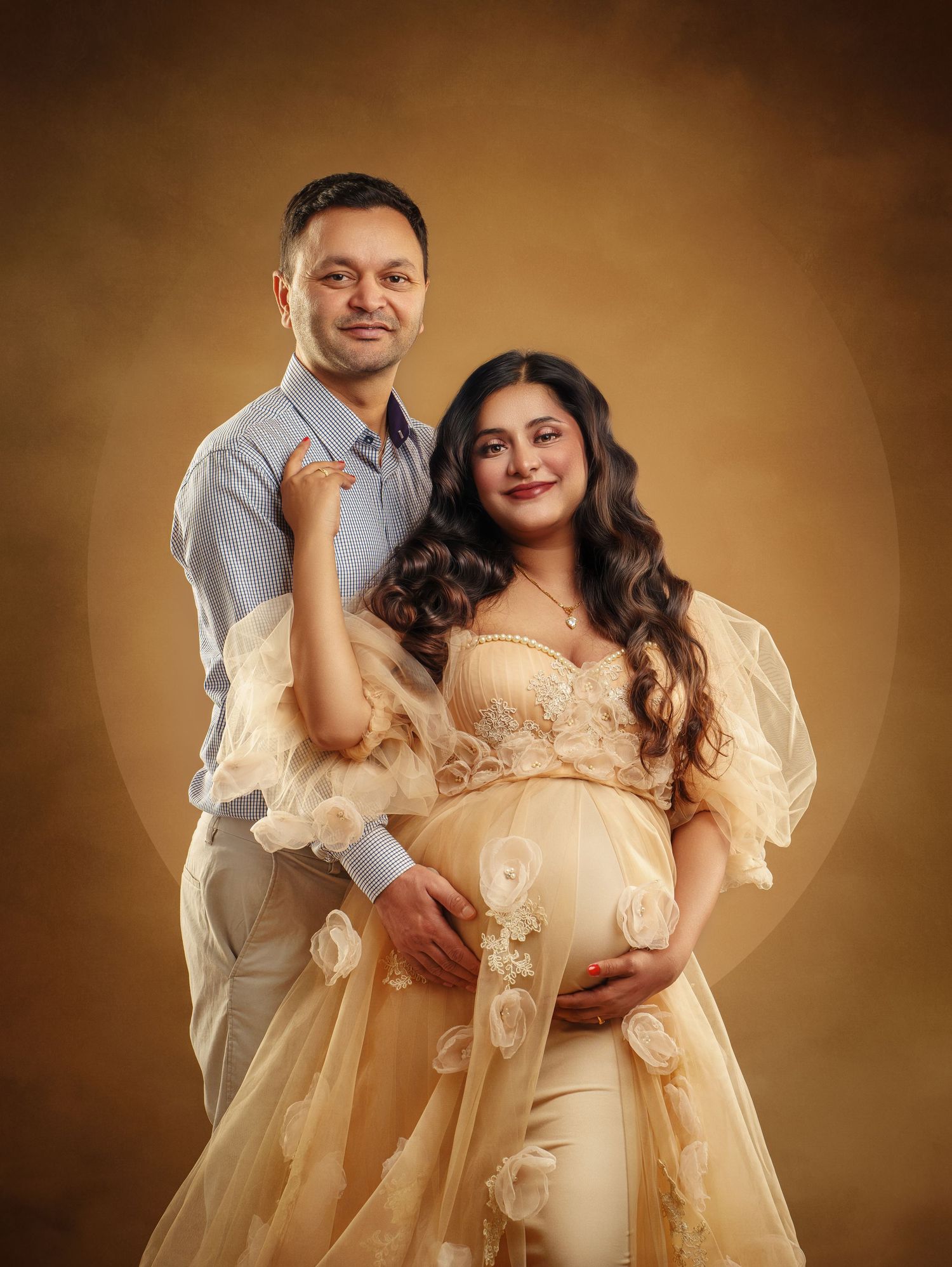 Couple poses for a maternity photo in traditional Indian-inspired attire against a warm brown backdrop.