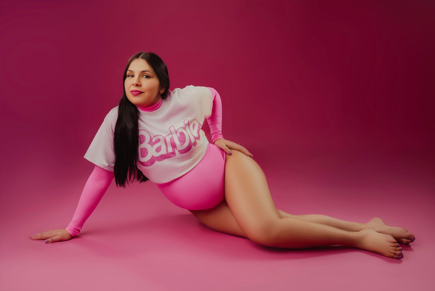 Model poses in pink bodysuit and shirt on pink background during fashion photoshoot.