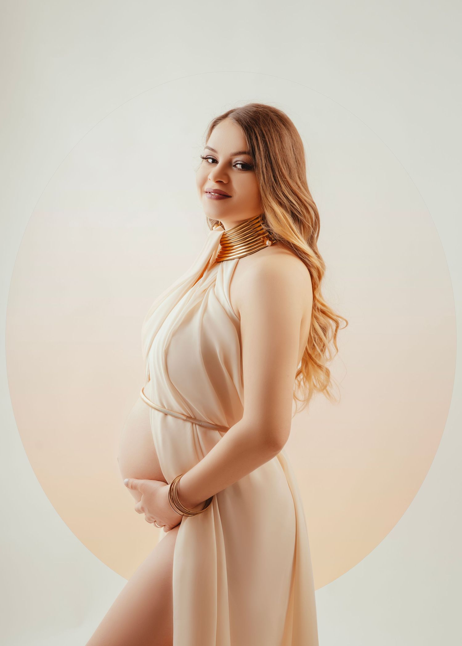 A minimalist maternity photo featuring a person in a flowing cream-colored dress against a neutral background.