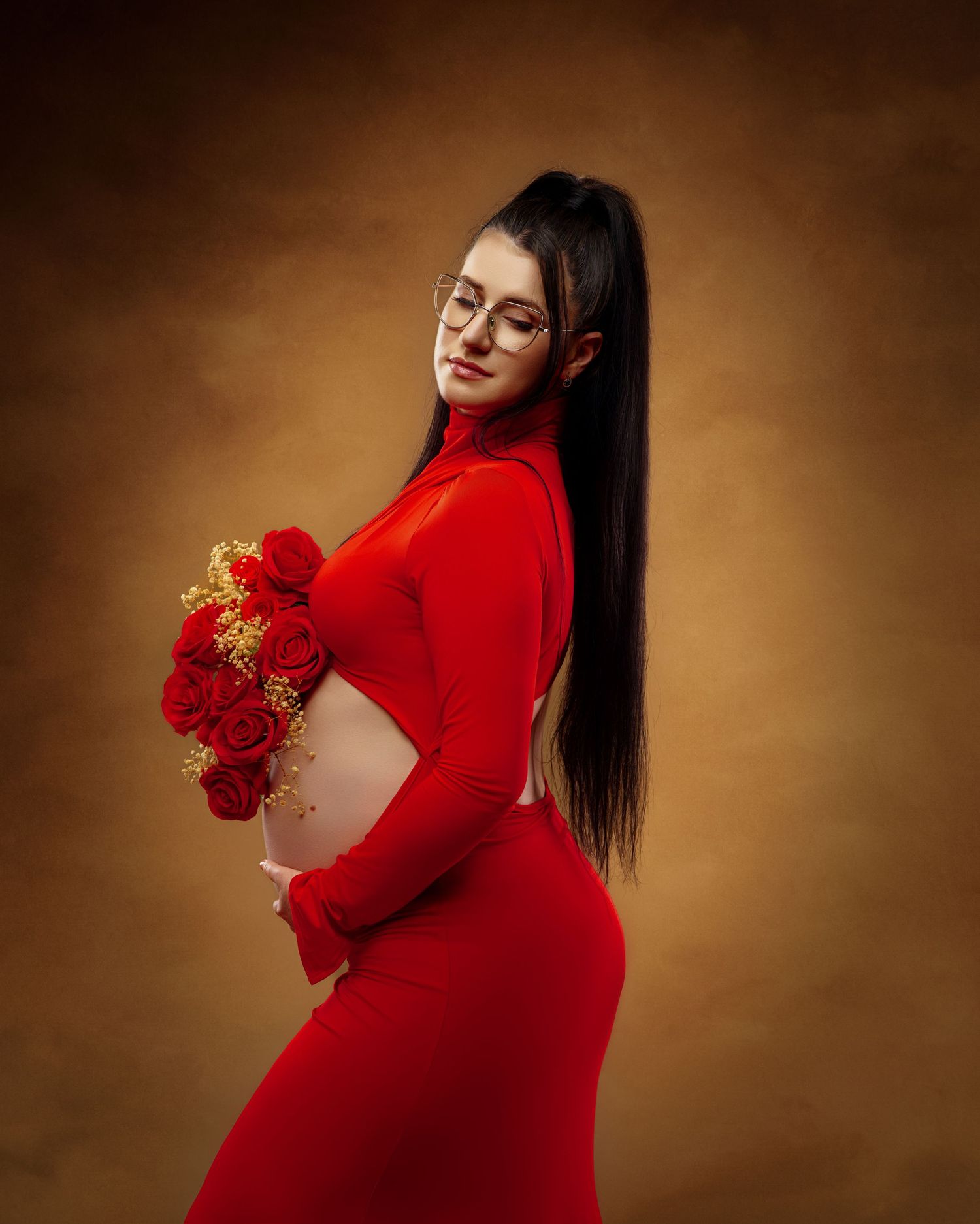 Maternity photoshoot in red dress with roses against brown backdrop showcases elegance and motherhood.