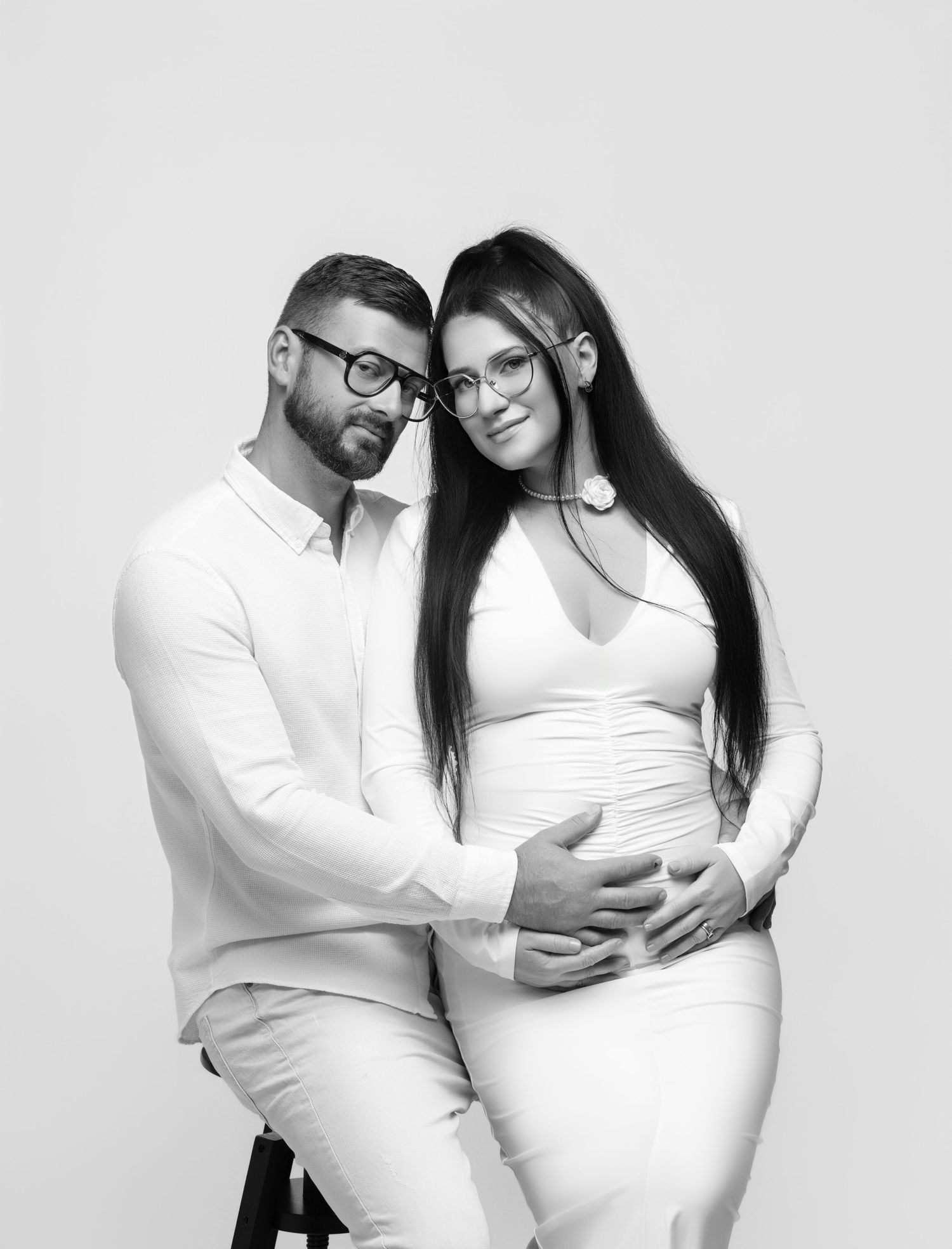 A black and white maternity photoshoot showing four tender poses of a couple in matching white outfits.