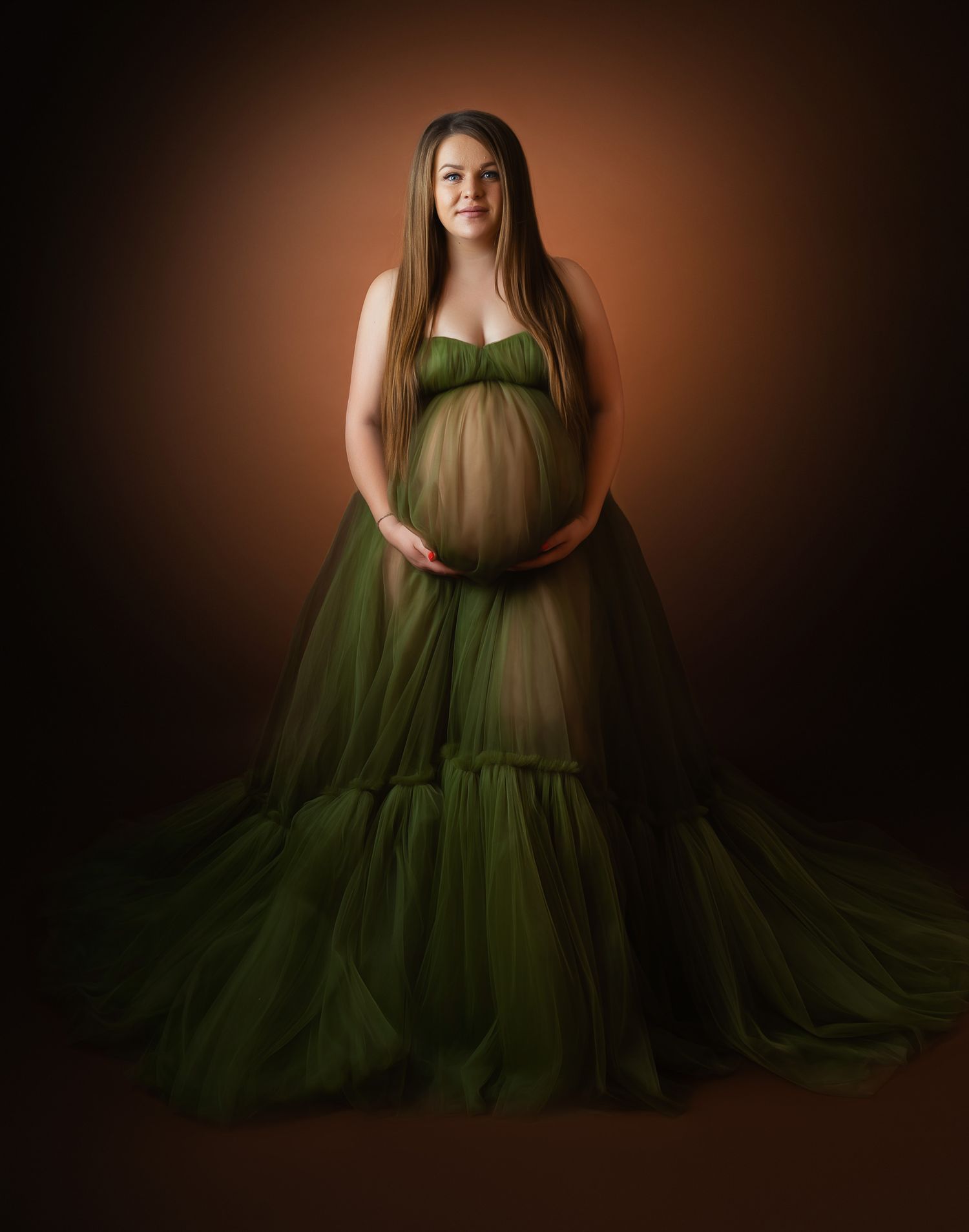 Maternity portrait showing an elegant olive green tulle gown against a dark brown backdrop.