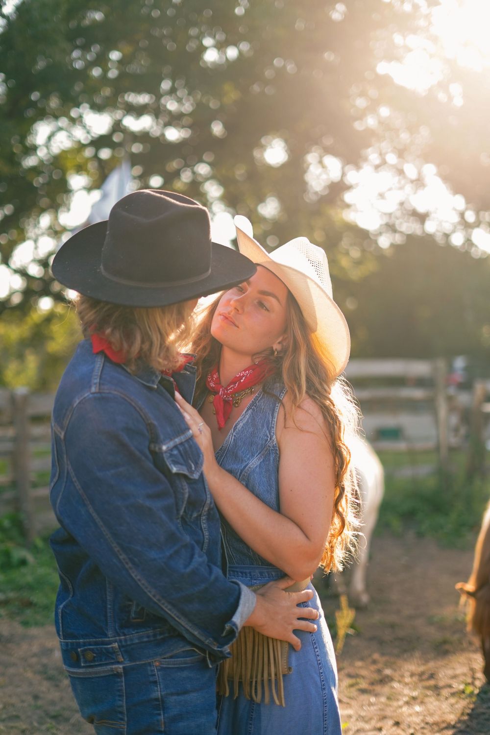Romantic couple in western wear embracing at sunset on a ranch.