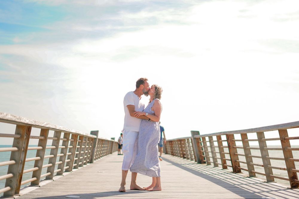A romantic moment captured on a wooden pier by the ocean at sunset.
