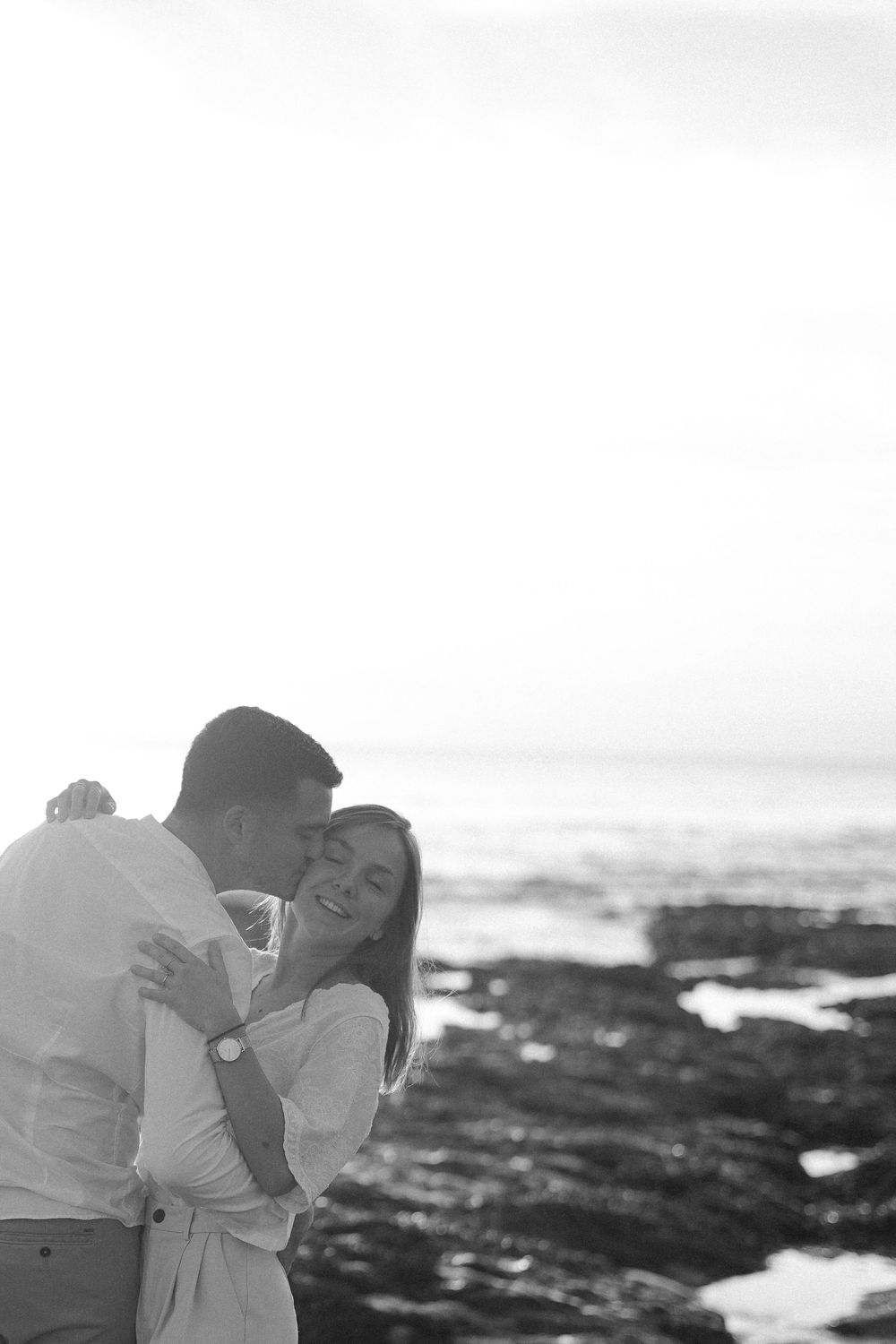 A romantic black and white portrait of a couple by the ocean rocks.