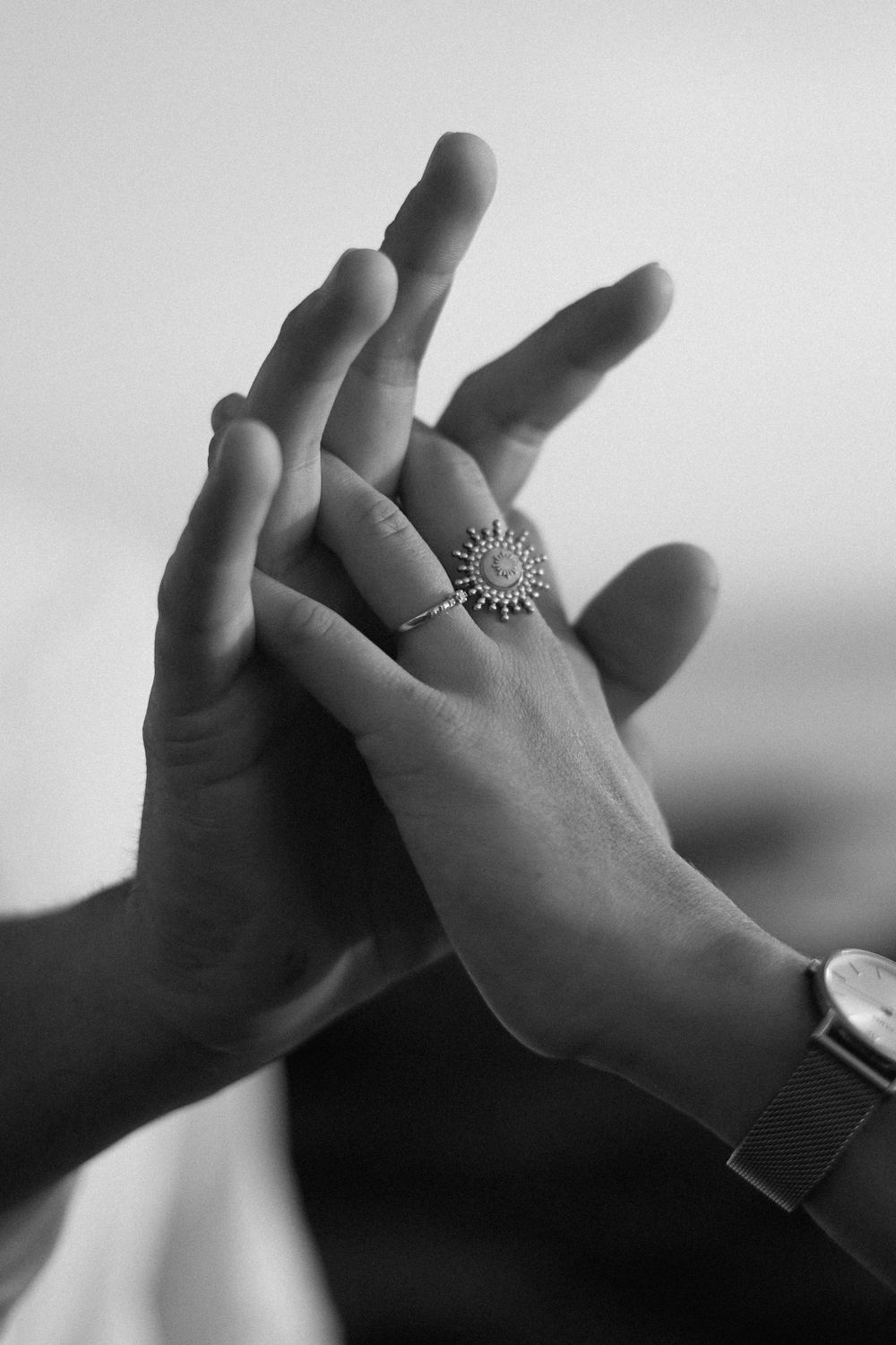 Black and white close-up of hands touching with decorative sun ring jewelry.
