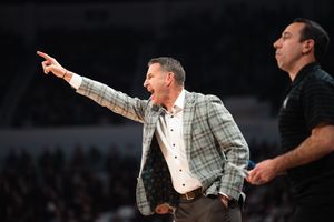 Animated college basketball coach in plaid jacket gestures and shouts instructions during a game.