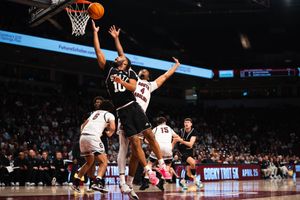 Basketball player drives to the hoop for a layup during a competitive college basketball game.