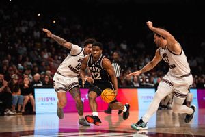 Kansas State basketball player dribbles past two Mississippi State defenders during an intense college basketball game.