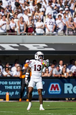 Wide shot of football players lined up on the field with a crowded stadium in the background.