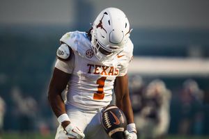Texas Longhorns football players in white uniforms running with the ball during gameplay.