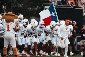 Texas Longhorns football team celebrates on the field during a game wearing their white uniforms.
