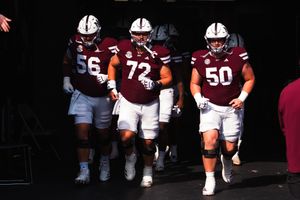Football players in maroon and white uniforms walking onto the field before a game.
