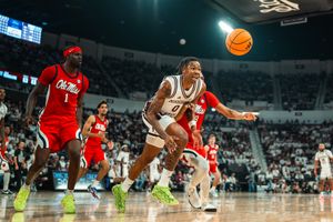 College basketball players chase a loose ball during an intense NCAA game in a packed arena.
