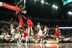 Players compete near the basket during an intense college basketball game in a packed arena.