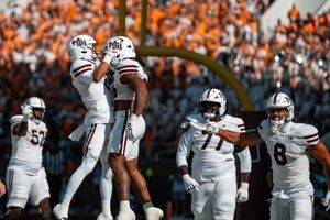 Football team in white uniforms huddling together on the field during a game.
