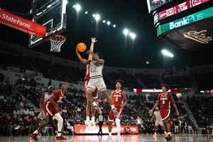 College basketball player #12 drives to the basket during an indoor arena game with fans in the background.