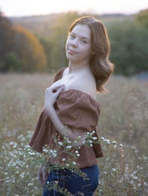 A portrait in a field at golden hour wearing a brown off-shoulder top.
