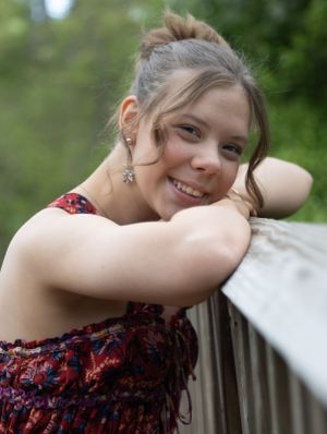 Portrait of someone in a floral dress leaning on an outdoor railing with a natural background.