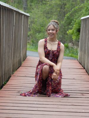 Someone in a floral dress poses sitting on a wooden bridge outdoors.