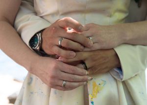 Close-up of hands wearing wedding rings resting on a floral patterned dress.
